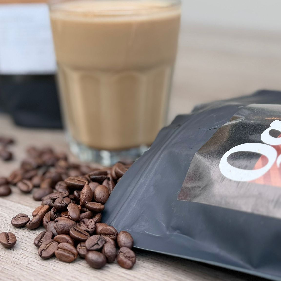 Glass of coffee, coffee beans, and a coffee package on a wooden surface.
